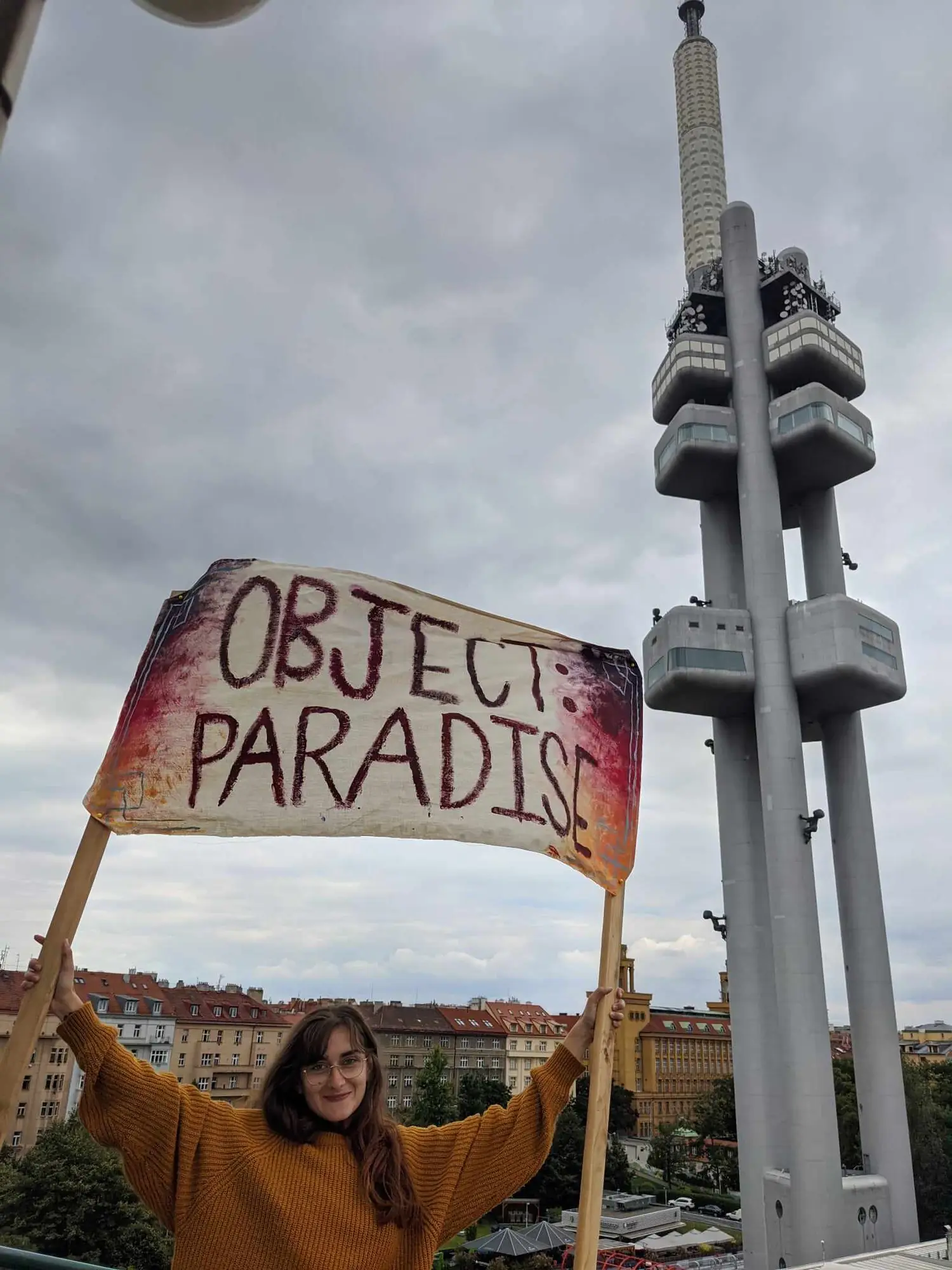 Sandra Pasławska holding the OBJECT:PARADISE banner before the Žižkov television tower